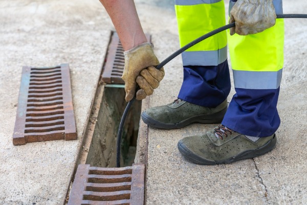 worker cleaning storm drain with cable